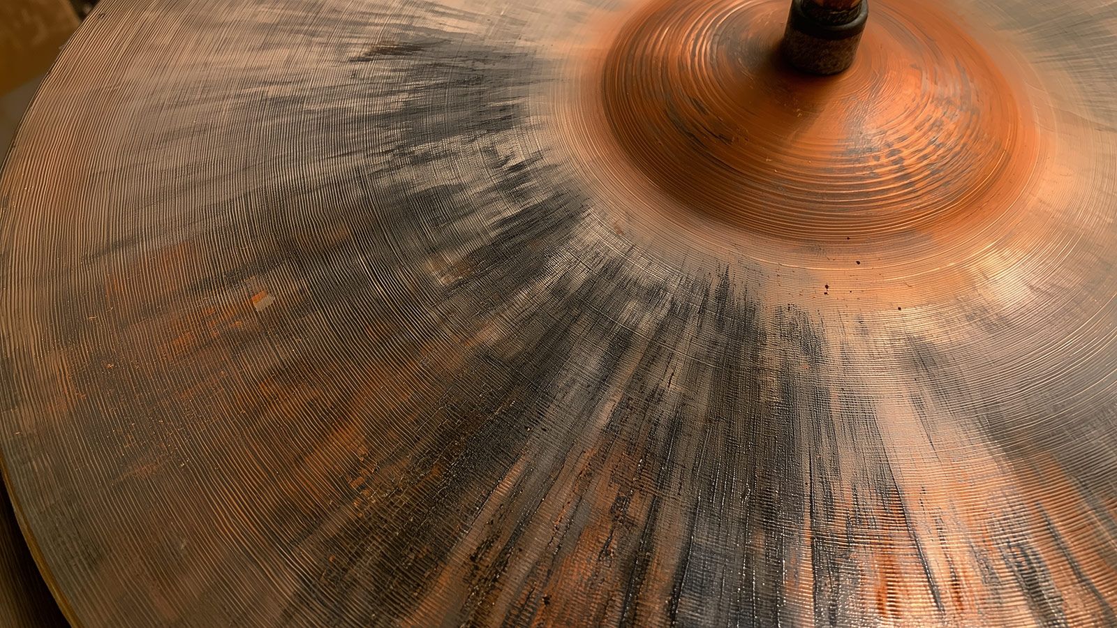 A close-up of a worn hi-hat cymbal, its surface showing hammering marks, stick wear, and light scratches across the metal.