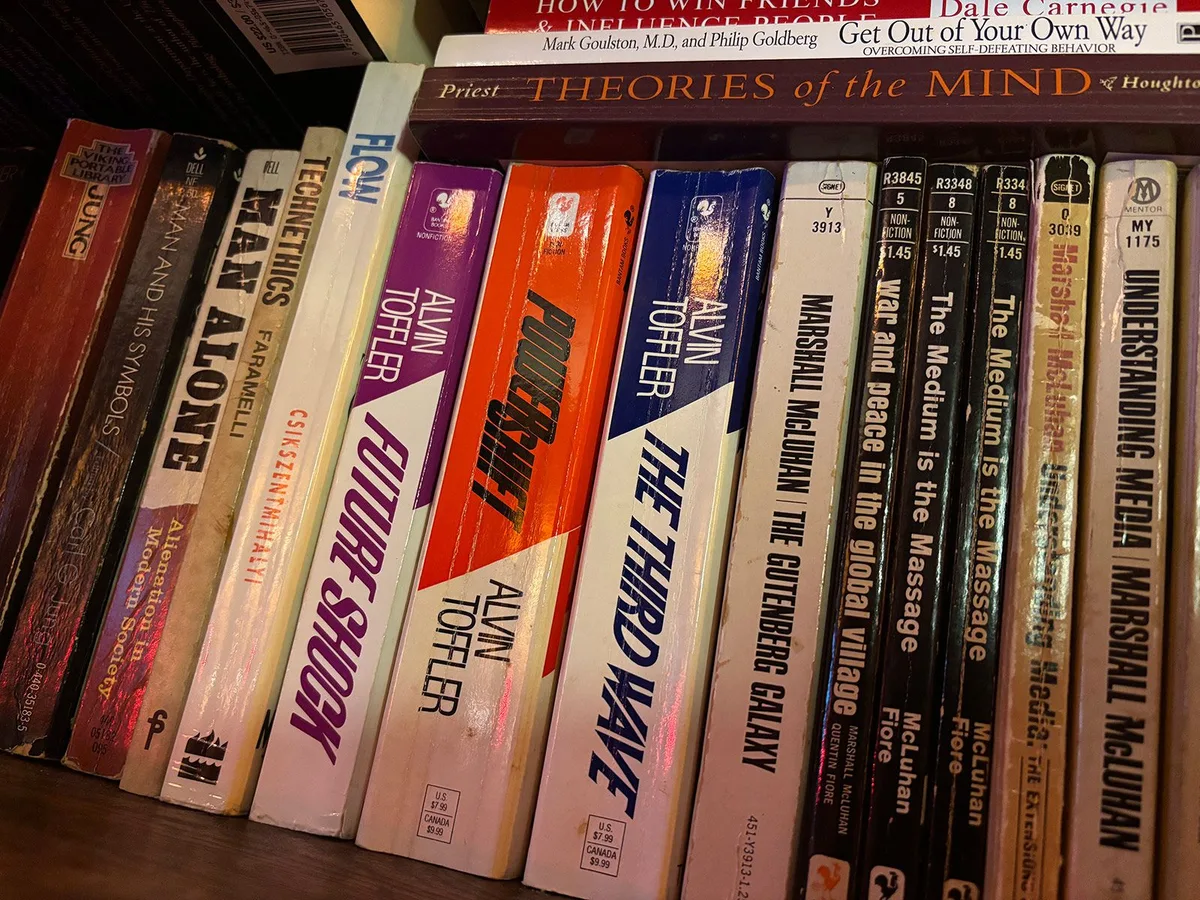 A row of well-worn paperbacks on a shelf, including several by Alvin Toffler (Future Shock, PowerShift, The Third Wave) and Marshall McLuhan (The Medium Is the Massage, Understanding Media).