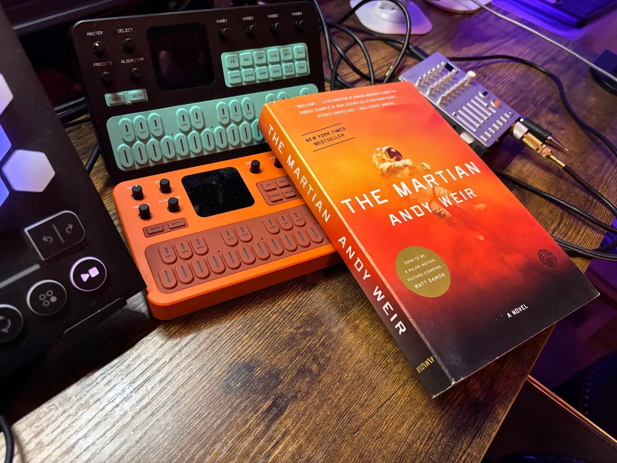 A paperback copy of Andy Weir’s The Martian leaning against a small FM synthesizer on a studio desk.